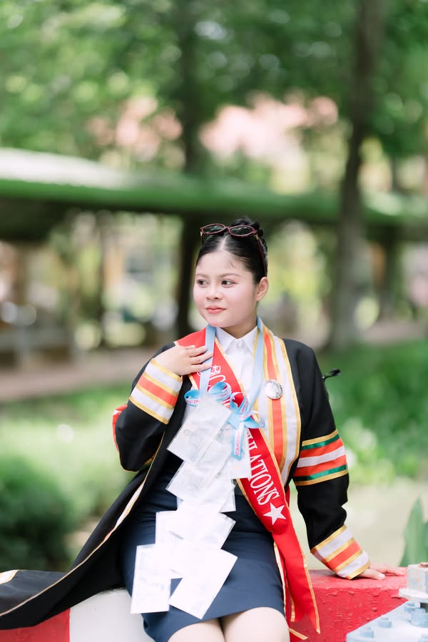 บัณฑิตหญิงในชุดครุยและสายสะพาย ท่ามกลางสวน